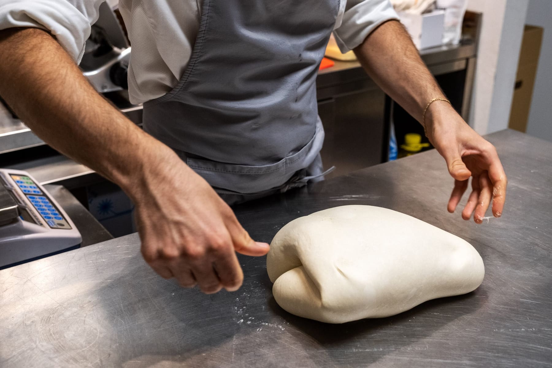 Due mani lavorano l'impasto sul banco d'acciaio della cucina, infarinato